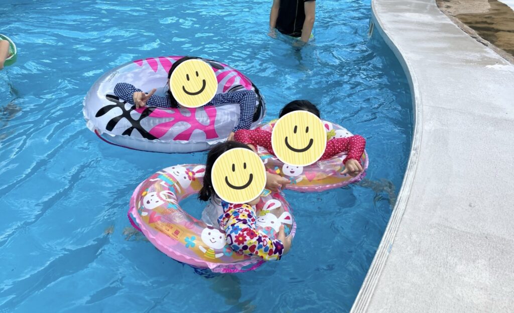 プールで３人の子供が浮き輪で浮かぶ写真