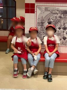 ピザ屋さんのコスチュームを着た半袖の３人の女の子が椅子に座っている